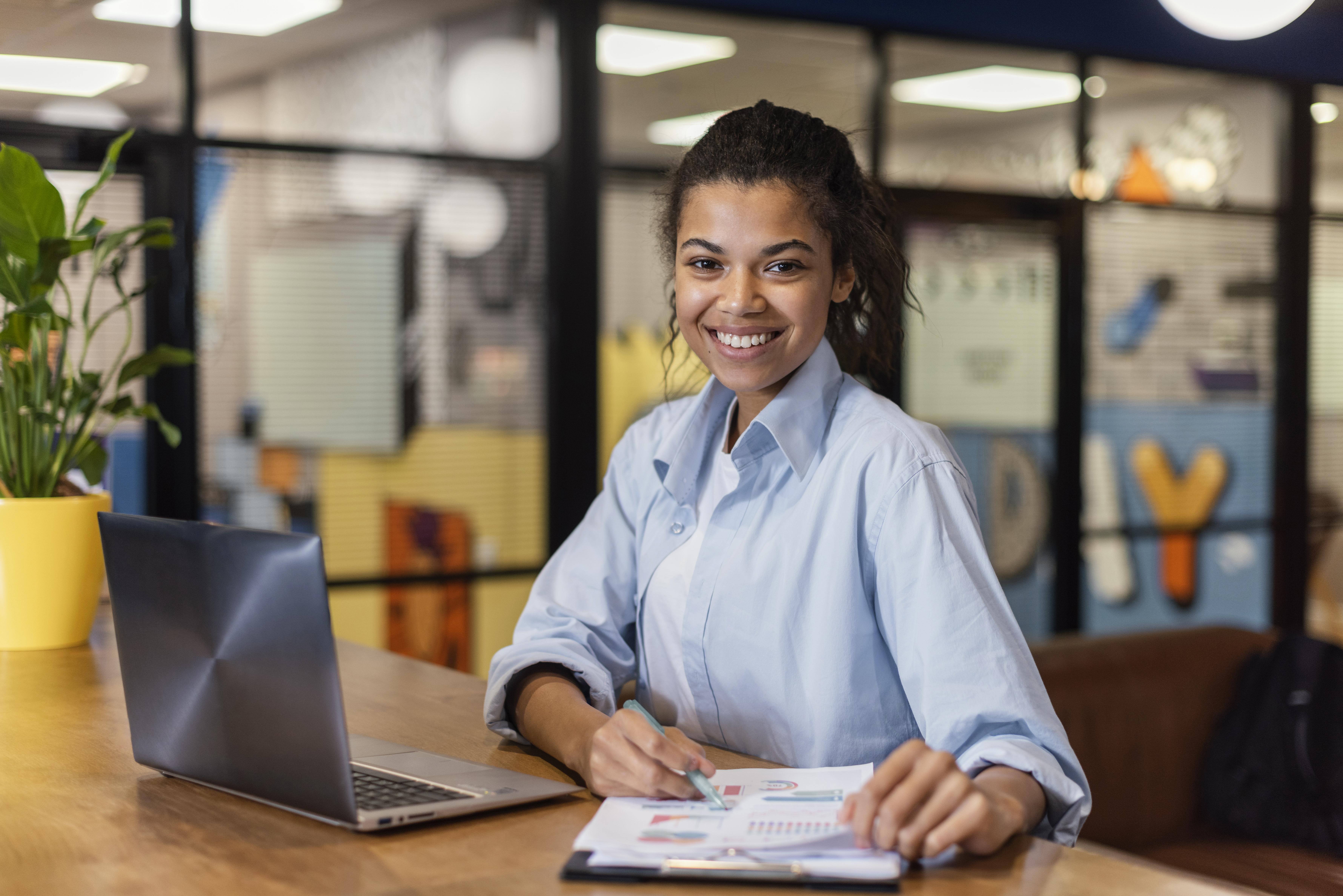 mujer-sonriente-trabajando-ordenador-portatil-papeles-oficina