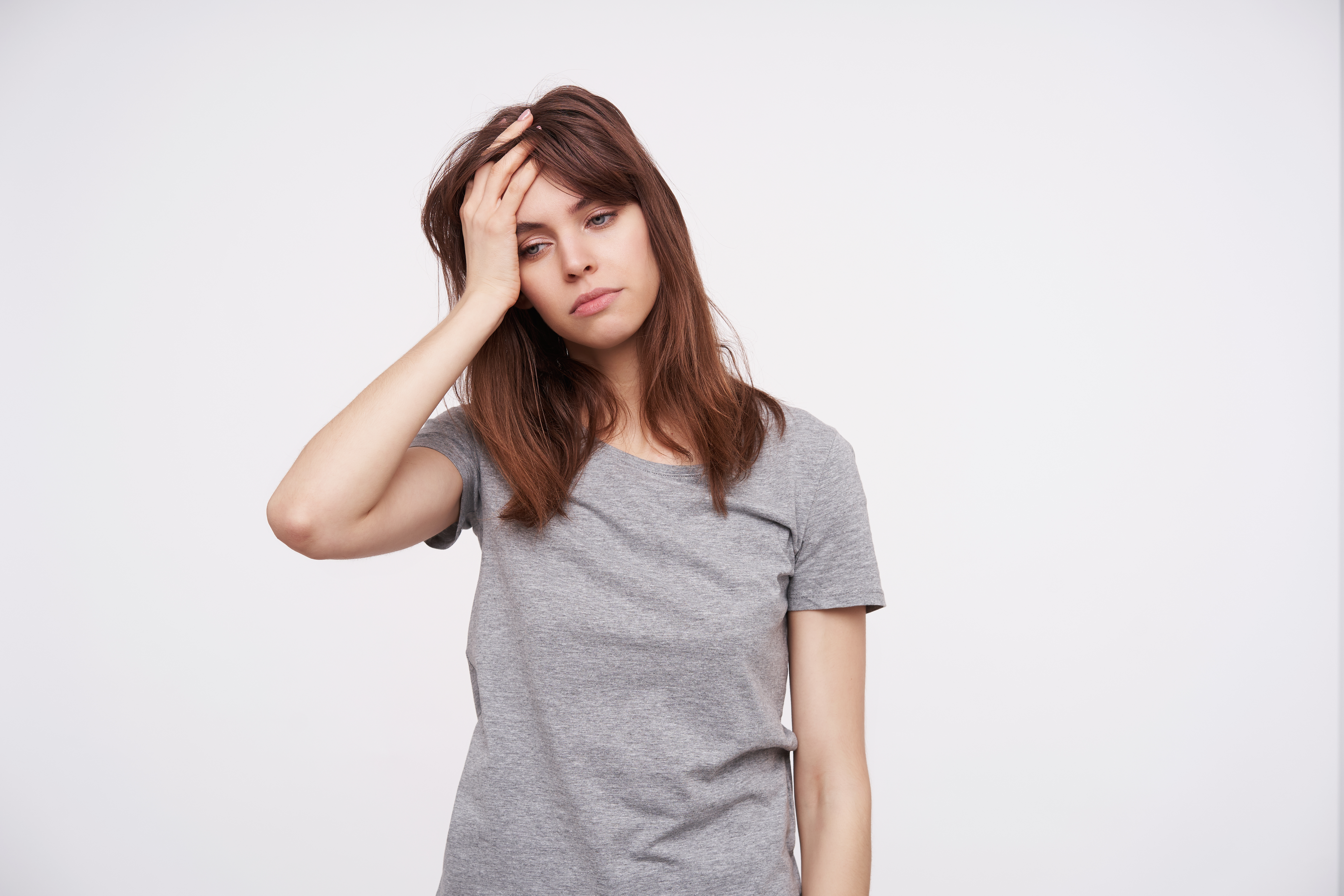 indoor-shot-young-pretty-brunette-female-holding-raised-hand-her-head-looking-tiredly-down-while-standing-white-background-casual-clothes