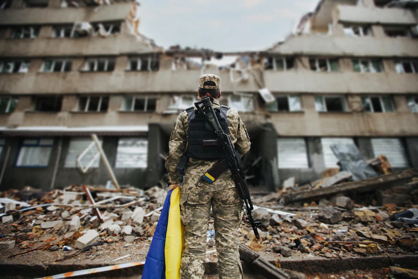 ukrainian-military-woman-with-the-ukrainian-flag-in-her-hands-on-the-background-of-an-exploded-house_219766-5938